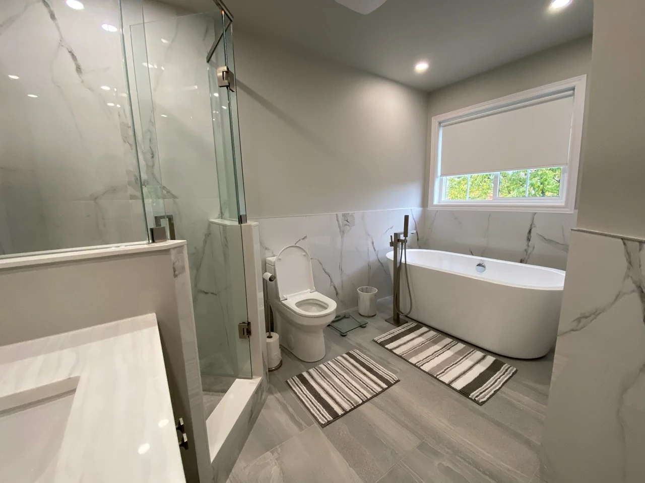 Bathroom with a freestanding bath below a window, a separate angled glass shower and grey floor tile