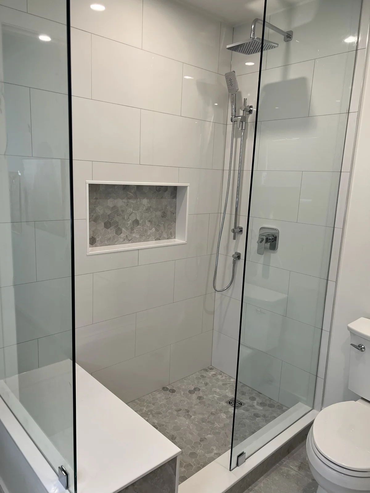 Glass shower with chrome fittings, a built-in bench and grey hexagonal mosaic in the niche and on the floor