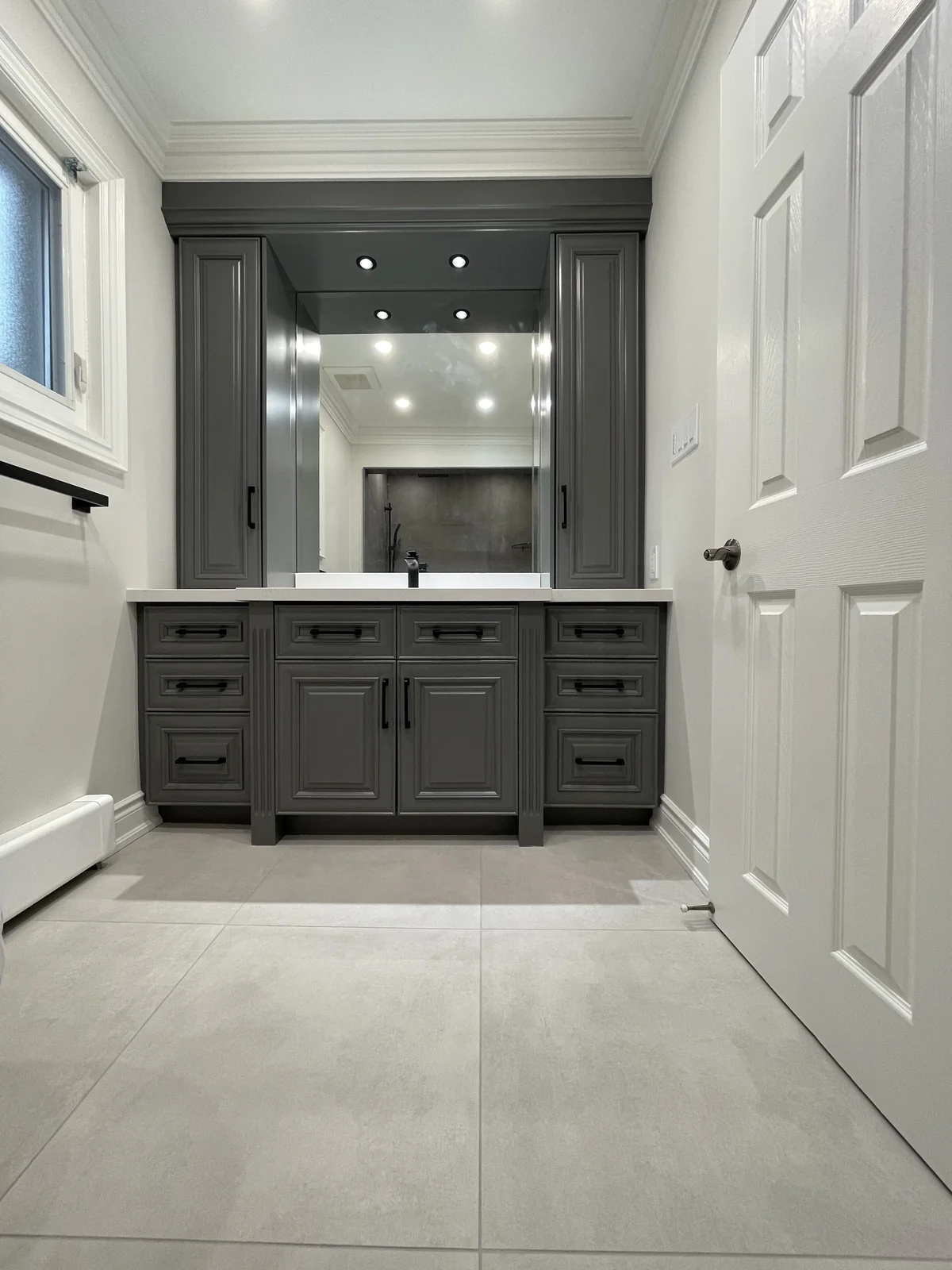 Graphite-coloured vanity with drawers, tall cupboards flanking the mirror and small lights above