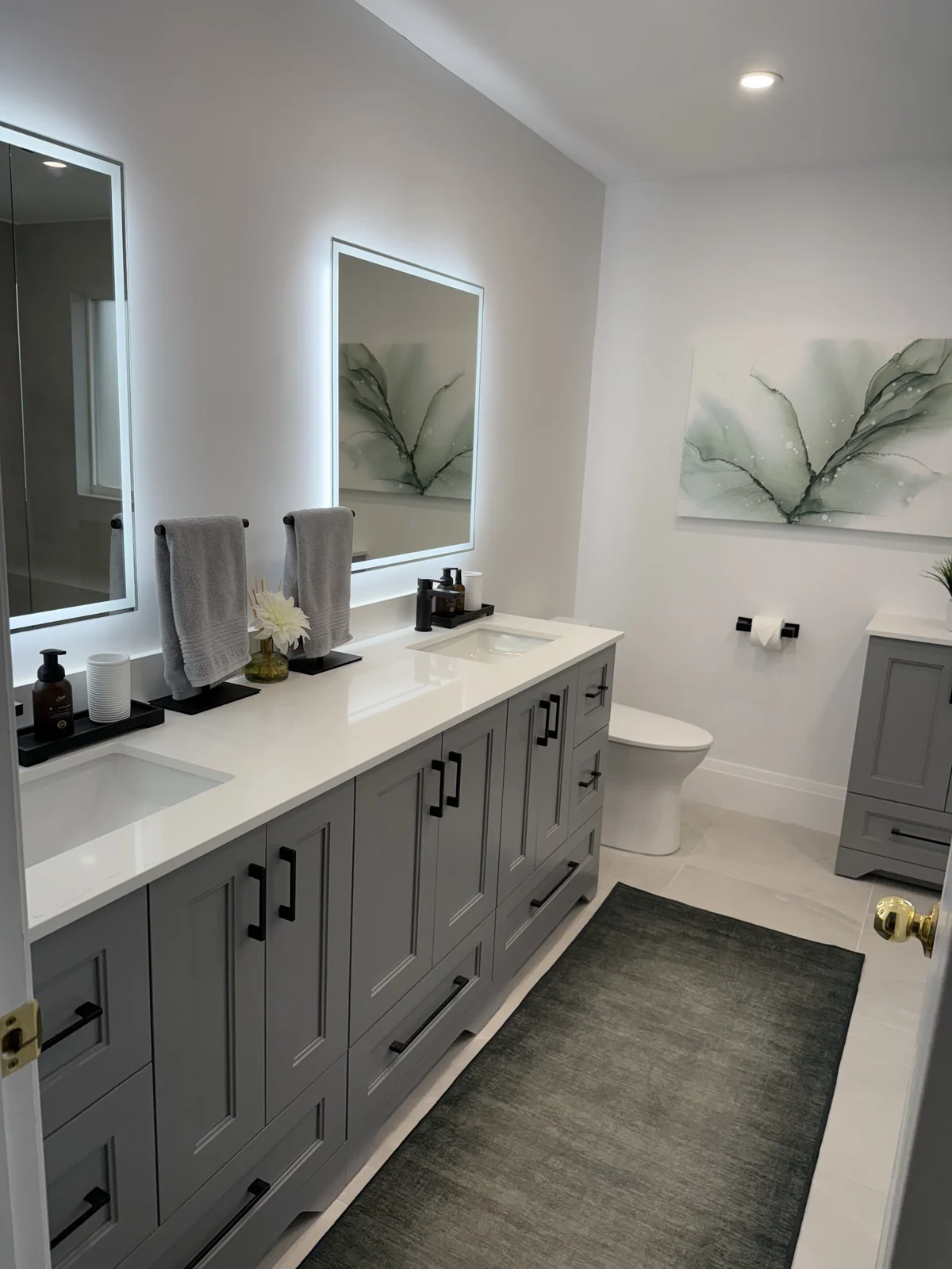 Grey double vanity with black handles and taps, two illuminated rectangular mirrors and coordinated towels and accessories