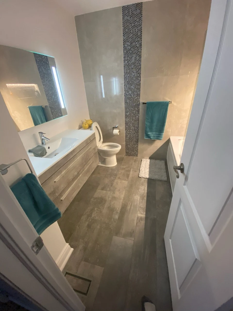 Bathroom with a wood-tone drawer vanity, illuminated mirror, mosaic accent strip and built-in bath