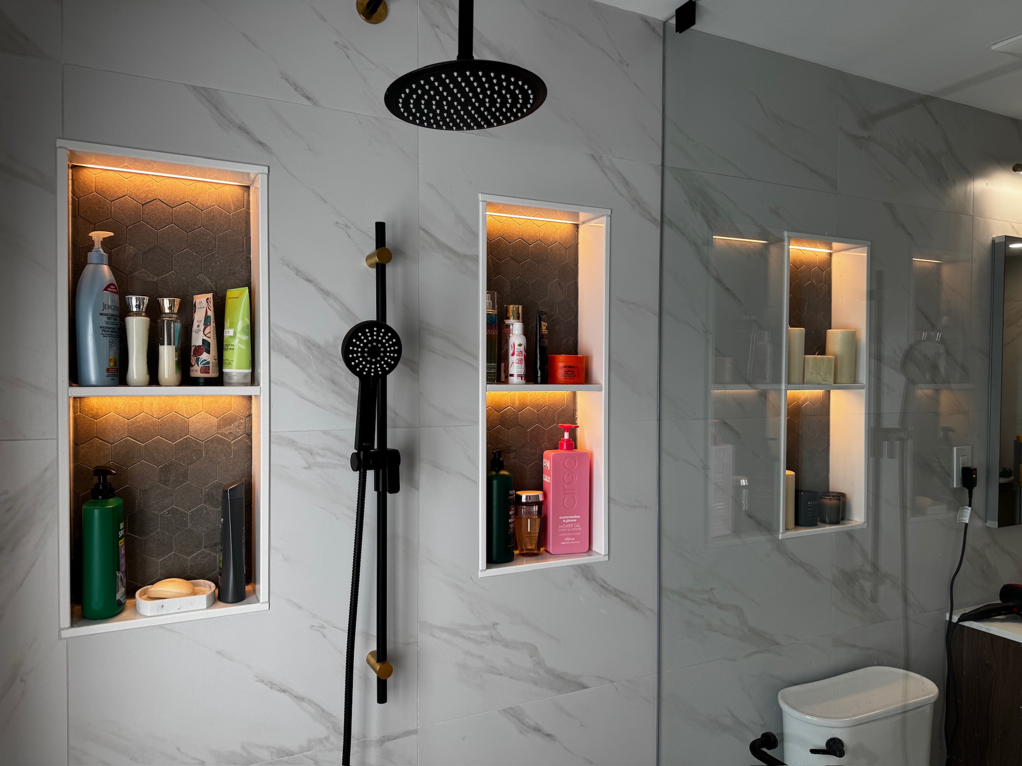 Rain shower and warm-lit tile niches in a finished bathroom