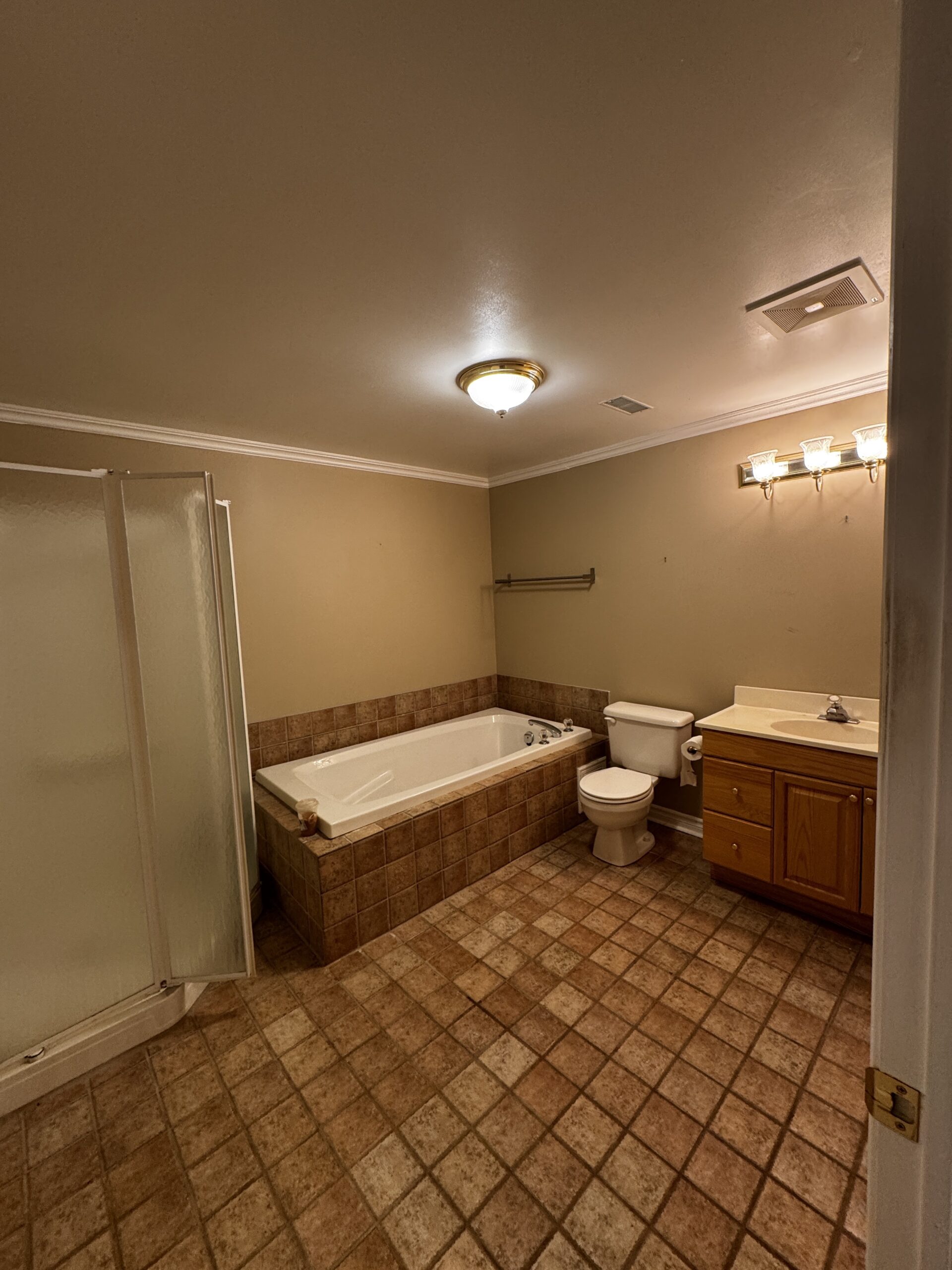Before bathroom renovation in Erin Mills, Mississauga: a separate shower, built-in bathtub, wood-tone vanity and brown square floor tiles.
