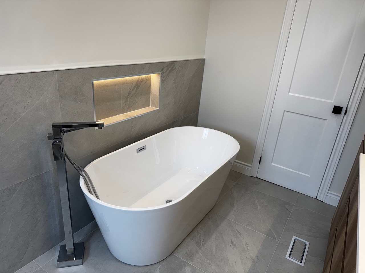 White freestanding bathtub with a floor-mounted filler and illuminated wall niche in Erin Mills