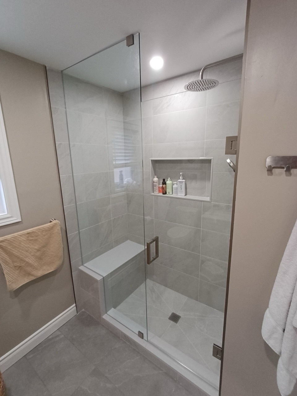 Glass-enclosed shower with grey tile, a bench and recessed niche in Erin Mills
