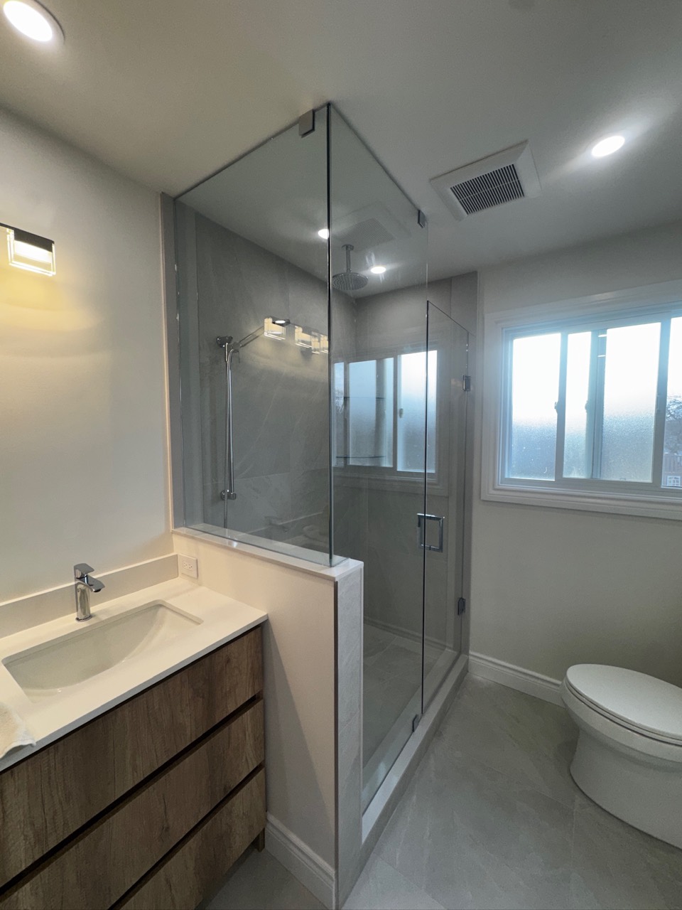 Wood-tone vanity beside a glass shower and frosted window in an Erin Mills bathroom